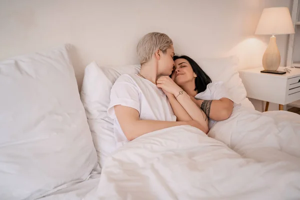 Jeune couple lesbien couché au lit, souriant et tenant la main — Photo de stock