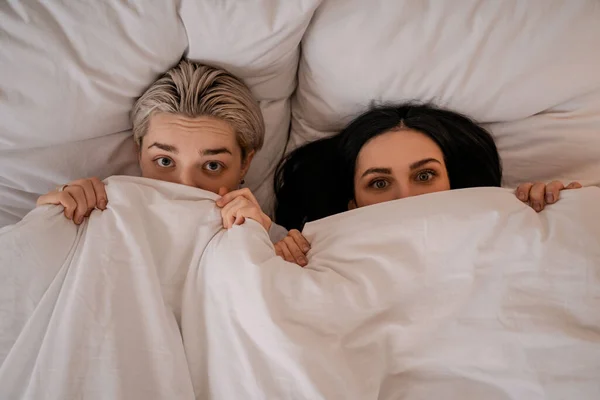 Vista superior de la joven pareja lesbiana tumbada en la cama debajo de la manta - foto de stock