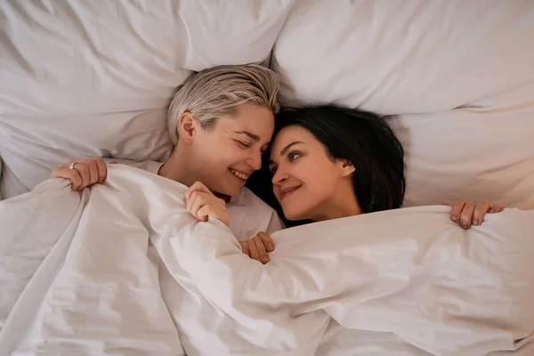 Vista superior de feliz pareja de lesbianas tumbados en la cama debajo de la manta - foto de stock