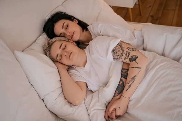 High angle view of young lesbian couple lying in bed and holding hands — Stock Photo
