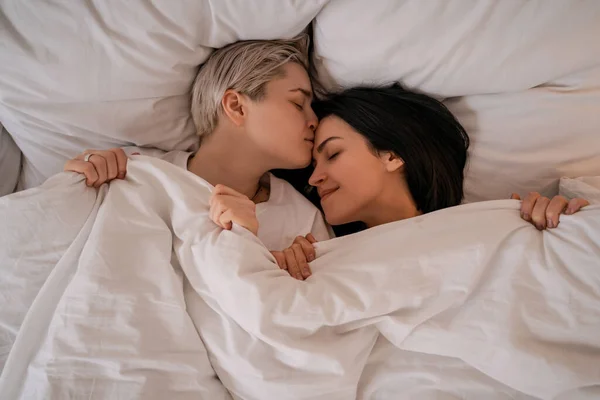 Vista superior de pareja lesbiana tumbada en la cama debajo de la manta - foto de stock