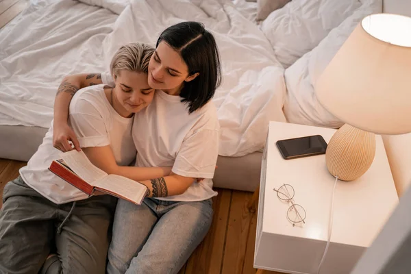 Blick aus der Vogelperspektive auf ein glückliches junges lesbisches Paar, das Buch im Schlafzimmer liest — Stockfoto
