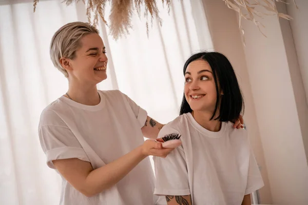 Allegra giovane donna spazzolando i capelli della ragazza bruna in camera da letto — Foto stock