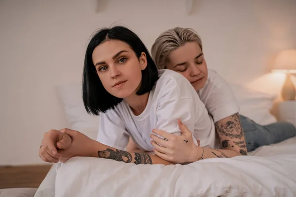 Young lesbian woman hugging tattooed girlfriend and lying on bed — Stock Photo