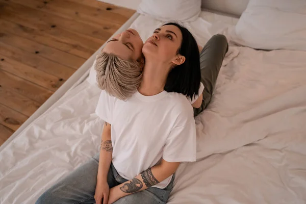 Alto ângulo vista de tatuado lésbicas casal sentado de volta para trás na cama — Fotografia de Stock