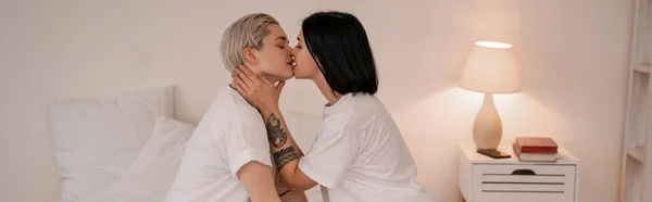 Vista lateral de pareja lesbiana besándose en el dormitorio, pancarta - foto de stock