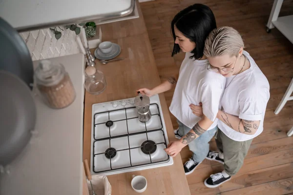 High angle view of young woman hugging girlfriend near coffee pot on stove — Stock Photo