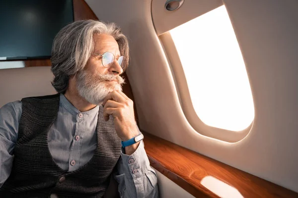 Reifer Mann mit Brille und Smartwatch blickt im Flugzeug auf Fenster — Stockfoto