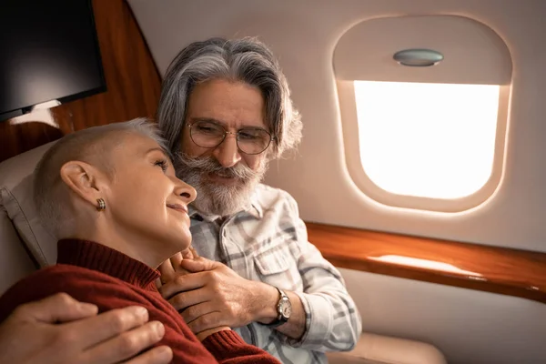 Зрілий чоловік обіймає усміхнену дружину в приватному літаку — стокове фото