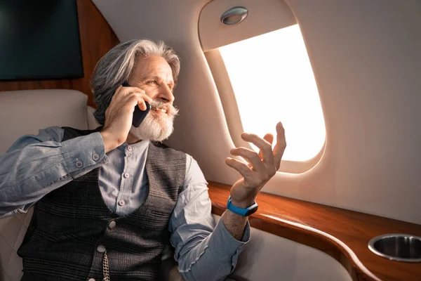 Smiling mature businessman talking on smartphone and looking at airplane window — Stock Photo