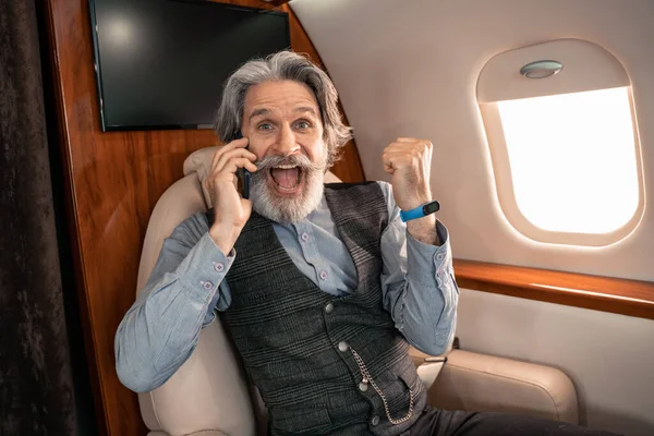 Emocionado hombre de negocios hablando en smartphone y mostrando sí gesto en avión — Stock Photo