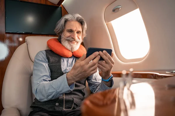 Улыбающийся бизнесмен в подушку на шее с помощью смартфона в самолете — стоковое фото