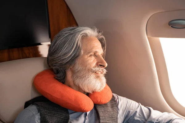 Smiling man in neck pillow looking at window in private plane — Stock Photo