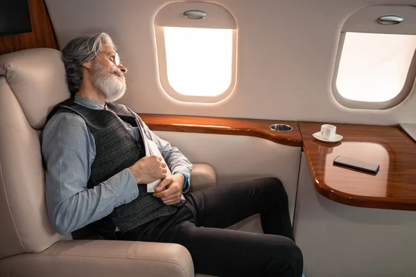 Reifer Geschäftsmann mit Magazin schläft neben Tasse und Smartphone im Jet — Stockfoto