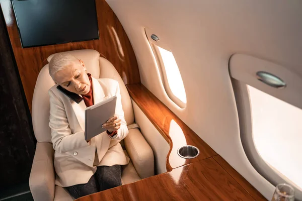 Businesswoman talking on smartphone and using digital tablet in private jet — Stock Photo