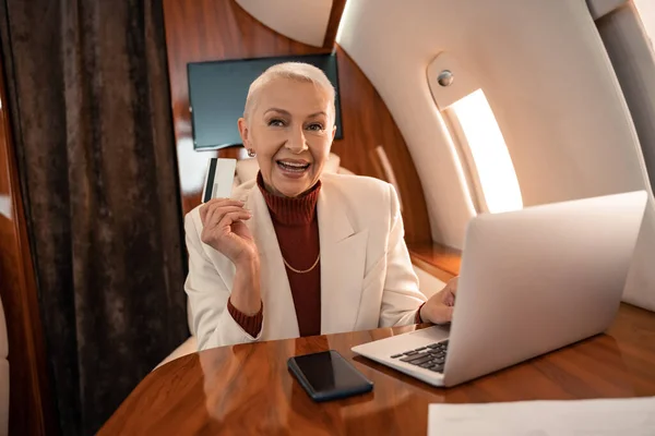 Smiling businesswoman holding credit card near devices in private jet — Stock Photo