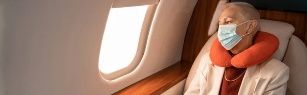 Зрелая деловая женщина в подушке для шеи и медицинская маска в самолете, баннер — стоковое фото