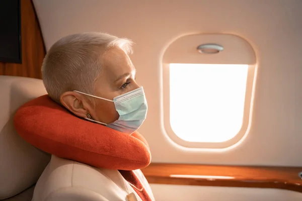 Бизнесмен в медицинской маске и подушке на шее сидит в самолете — стоковое фото