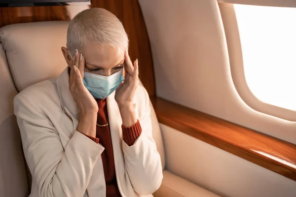 Imprenditrice in maschera medica che soffre di mal di testa in aereo — Foto stock