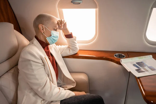 Бизнесмен в медицинской маске смотрит журнал в частном самолете — стоковое фото