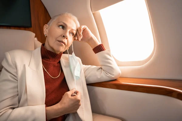 Mature businesswoman taking off medical mask in private jet — Stock Photo