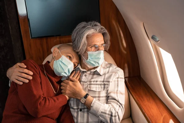 Mann mit medizinischer Maske umarmt Ehefrau im Privatjet — Stockfoto