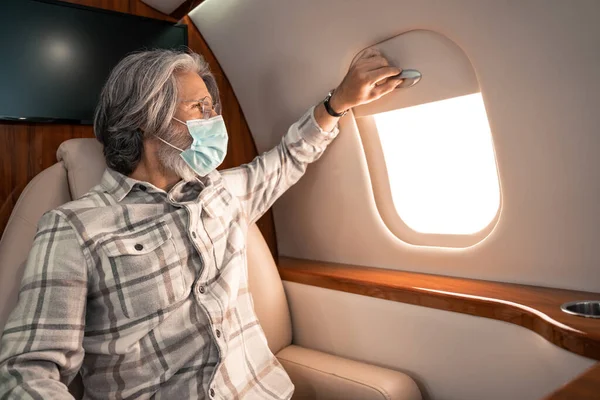 Uomo in maschera protettiva guardando la finestra in aereo privato — Foto stock