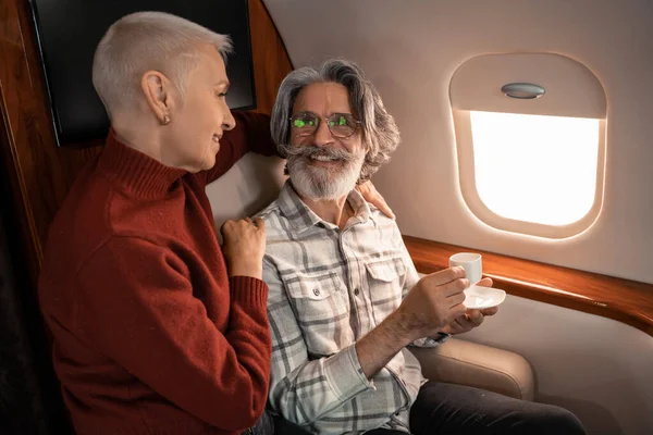 Mulher sorridente abraçando marido com café em avião privado — Fotografia de Stock