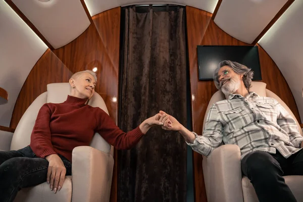 Cheerful couple holding hands in cabin of private jet — Stock Photo