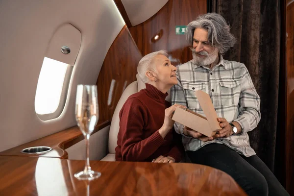 Усміхнена жінка тримає подарунок біля чоловіка і розмите шампанське в літаку — стокове фото