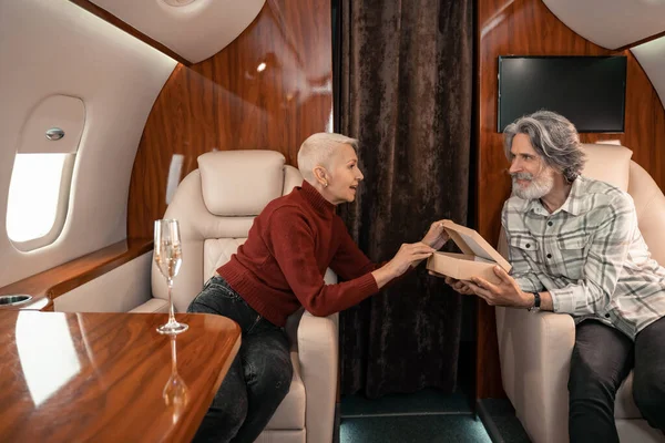 Smiling man holding present near wife and champagne in private jet — Stock Photo