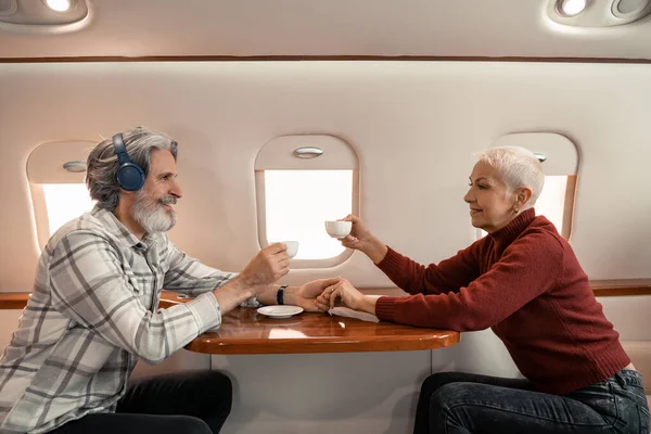 Vista lateral del hombre en auriculares mirando a la esposa con café en avión privado - foto de stock