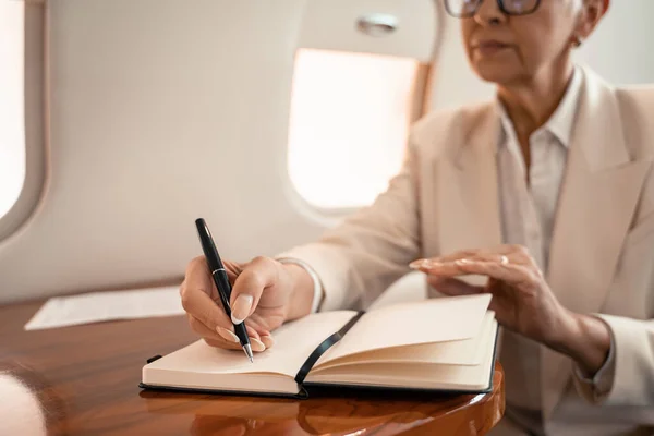 Vista recortada de la mujer de negocios borrosa escribiendo en el cuaderno en jet privado - foto de stock