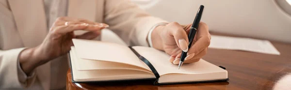 Cropped view of mature businesswoman writing on notebook in plane, banner — Stock Photo