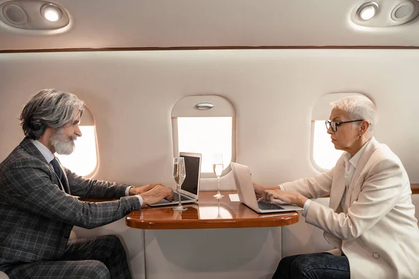 Side view of business people using laptops near champagne in private jet — Stock Photo