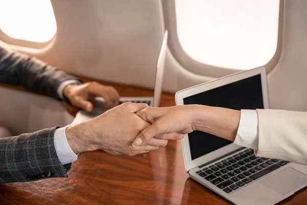 Cropped view of business people shaking hands near laptops in plane — Stock Photo