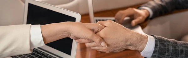 Vista ritagliata di uomini d'affari che stringono la mano vicino ai computer portatili in aereo privato, banner — Foto stock