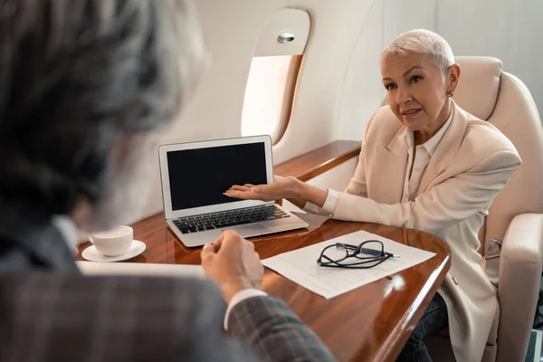 Empresária apontando com a mão para laptop perto de documento e empresário em avião — Fotografia de Stock