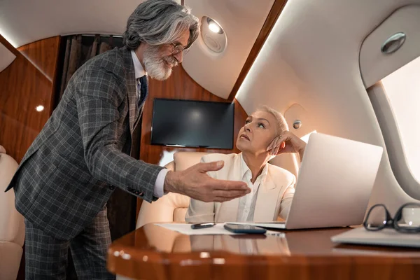 Smiling businessman pointing at laptop near paper and partner in private jet — Stock Photo