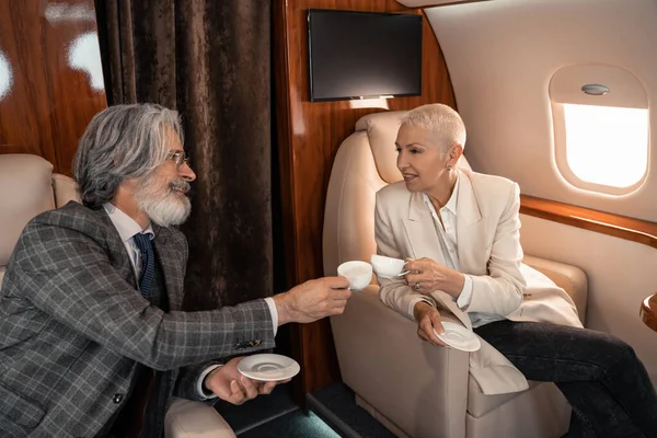 Cheerful business people clinking with coffee cups in private plane — Stock Photo