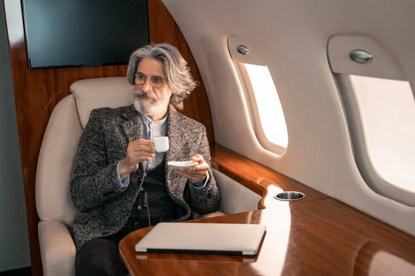Empresario sosteniendo café cerca de computadora portátil borrosa en avión privado — Stock Photo