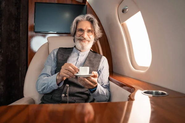 Uomo sorridente che tiene il caffè e guarda la fotocamera in aereo — Foto stock