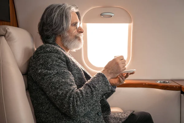 Side view of man in eyeglasses holding cup of coffee in private jet — Stock Photo