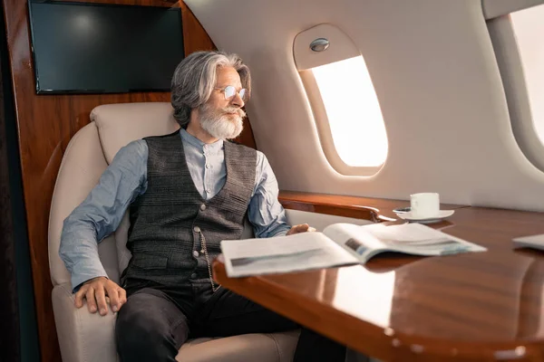 Зрілий чоловік дивиться на вікно біля журналу і кави в літаку — стокове фото