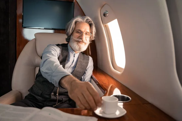 Улыбающийся бизнесмен пьет кофе возле журнала в самолете — стоковое фото