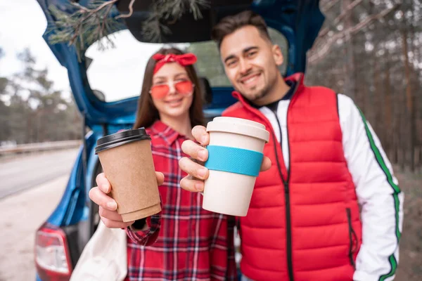 Blurred man and woman holding reusable and paper cups near car — Stock Photo