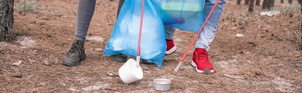 Partial view of couple with trash bags picking up rubbish with grabber tools in woods, banner — Stock Photo