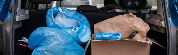 Caja de cartón con taza de papel cerca de bolsas de basura en coche moderno, pancarta - foto de stock