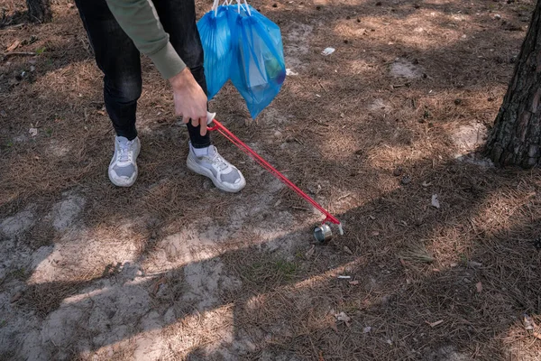 Vista recortada de voluntario sosteniendo recoger herramienta cerca de la basura en el bosque - foto de stock