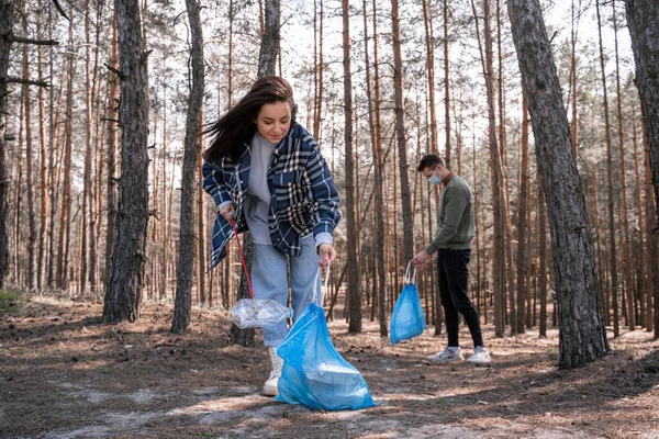 Junge Frau und Mann mit Müllsäcken sammeln Müll mit Greifwerkzeug im Wald auf — Stockfoto